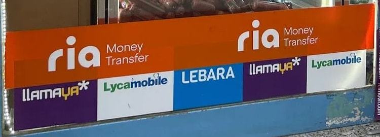 Franja del escaparate de Tienda Ouassim con los logotipos de Ria Money Transfer, Llamaya, Lycamobile y Lebara
