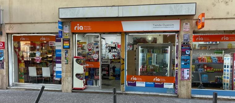 Façana de Tienda Ouassim al Carrer del Progrés, 5: el rètol taronja de Ria Money Transfer, el rètol blanc amb el nom de la botiga i els aparadors amb les marques de recàrregues