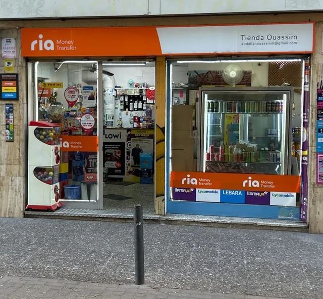 L'entrada de Tienda Ouassim: rètol taronja de Ria, la porta oberta i el rètol blanc amb el nom de la botiga